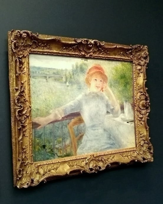 Uma jovem está sentada na varanda do restaurante Fournaise, apoiada numa mesa posta. Ela segura na mão cerejas penduradas na orelha. Ela usa um chapéu de palha com uma fita vermelha, da mesma cor do carmim que contorna sua boca sorridente. Seu cabelo é loiro. Seu braço direito estendido sobre a grade marca uma divisão com a paisagem ao fundo. Dá pra ver uma vela rápida navegando no rio Sena perto da ponte ferroviária.